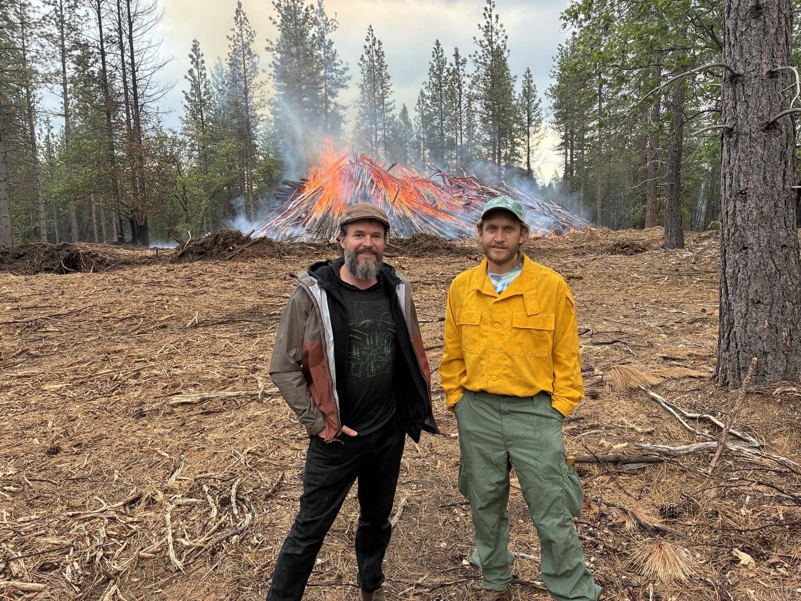 Chris Friedel and Theo Fitanides of Yuba Watershed Institute standing in front of an active machine pile burn.
