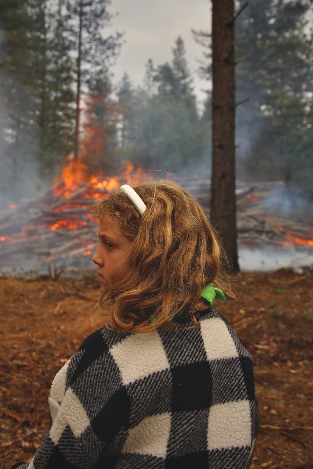 A young community member looks on as a machine pile smolders.